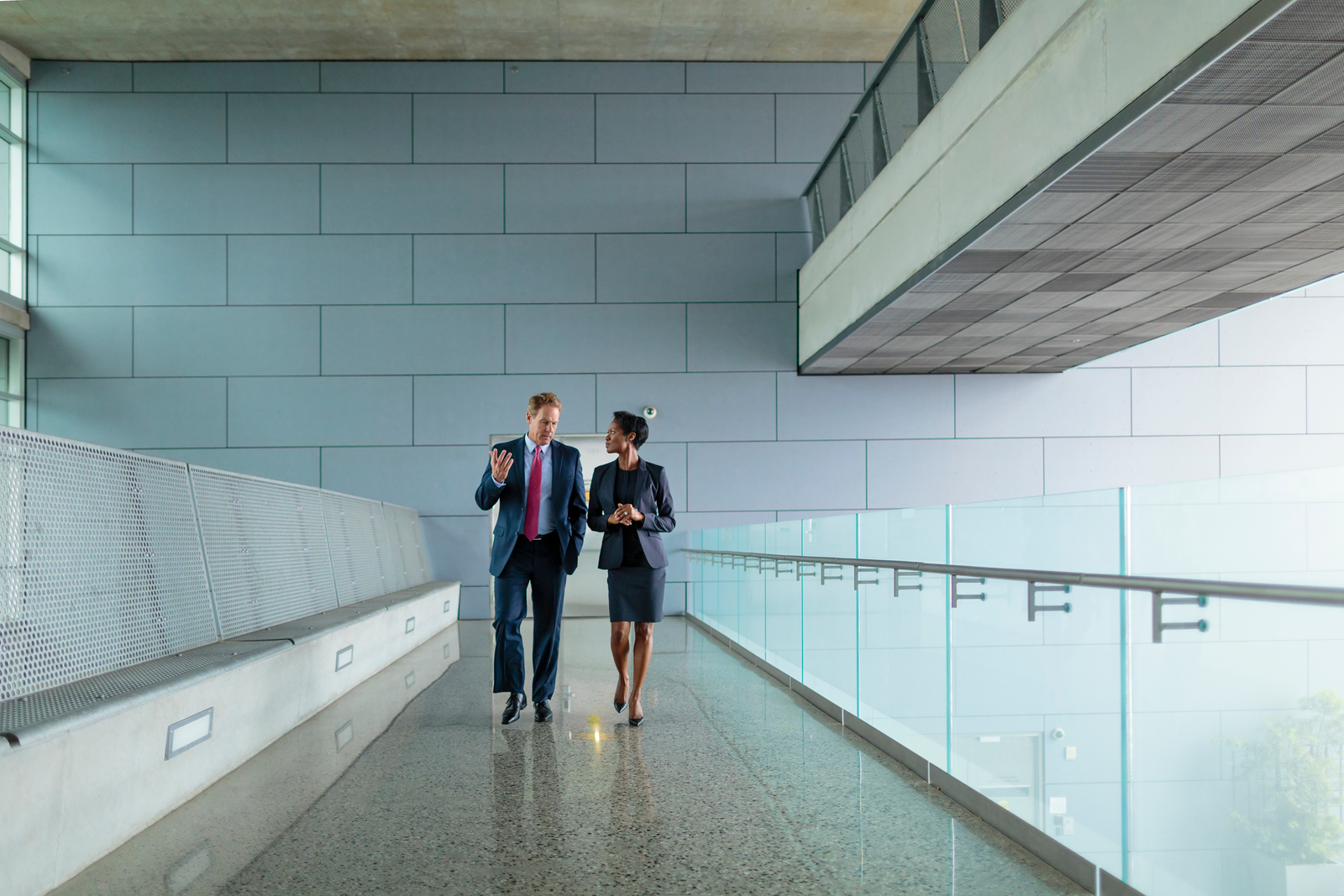 Businessman and businesswoman walking and talking on elevated walkway near modern office architecture